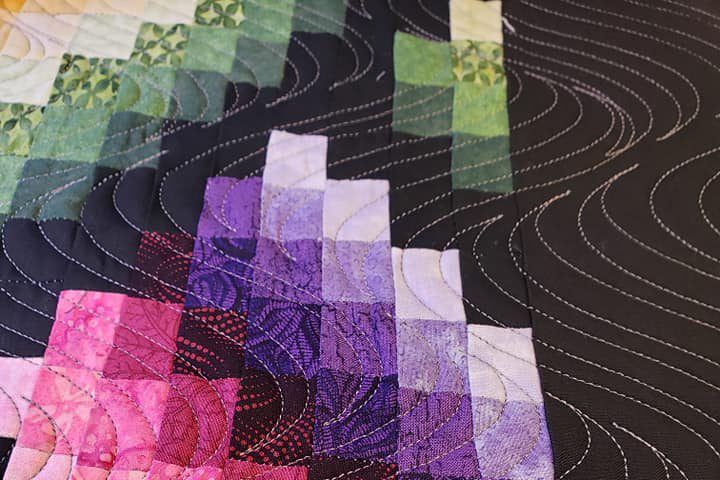 A close up of the quilt with purple and green squares.
